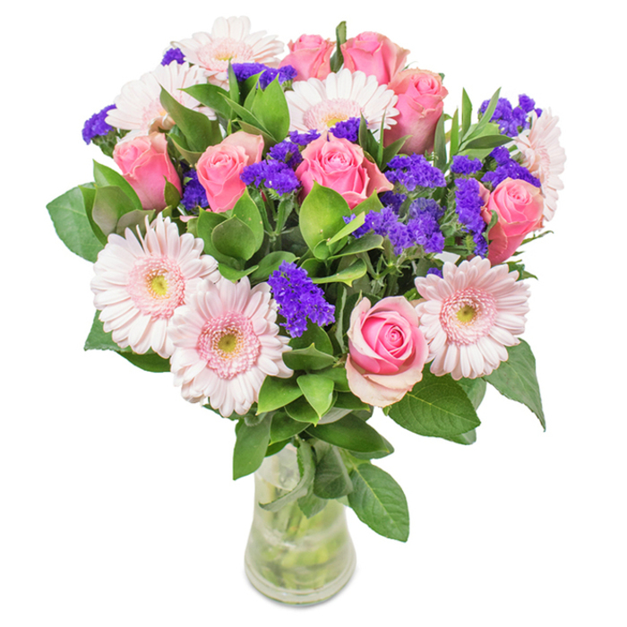 This elegantly curated floral arrangement stands out as a radiant centrepiece, captured within a pristine, clear glass vase set against a luminous white background, evoking the contemporary spirit of Walworth homes. Central to the bouquet are seven to nine sumptuous, medium-pink roses-some still unfurling, others starting to reveal their classic, tightly coiled spirals. Nestled among them, five to seven pale pink gerbera daisies bloom with broad, delicate petals and softly shimmering, nearly white centres-bringing a sense of youthful freshness. Clusters of striking purple statice are artfully woven throughout, lending sculptural form and bright punctuation reminiscent of vibrant shopfronts along Walworth Road. Lush, deep green foliage fills out the arrangement, each leaf adding fullness and referencing the leafy paths of Nursery Row Park. The clear vase, allowing a peek at the fresh stems and glinting water, reinforces the sense of just-arrived freshness and attention to detail for deliveries by Flowers Walworth. Suitable for birthdays, Mother's Day, anniversaries, or as an uplifting accent for a workspace, this bouquet is a testament to local artistry, expressing joy, celebration, and heartfelt connection at every glance.